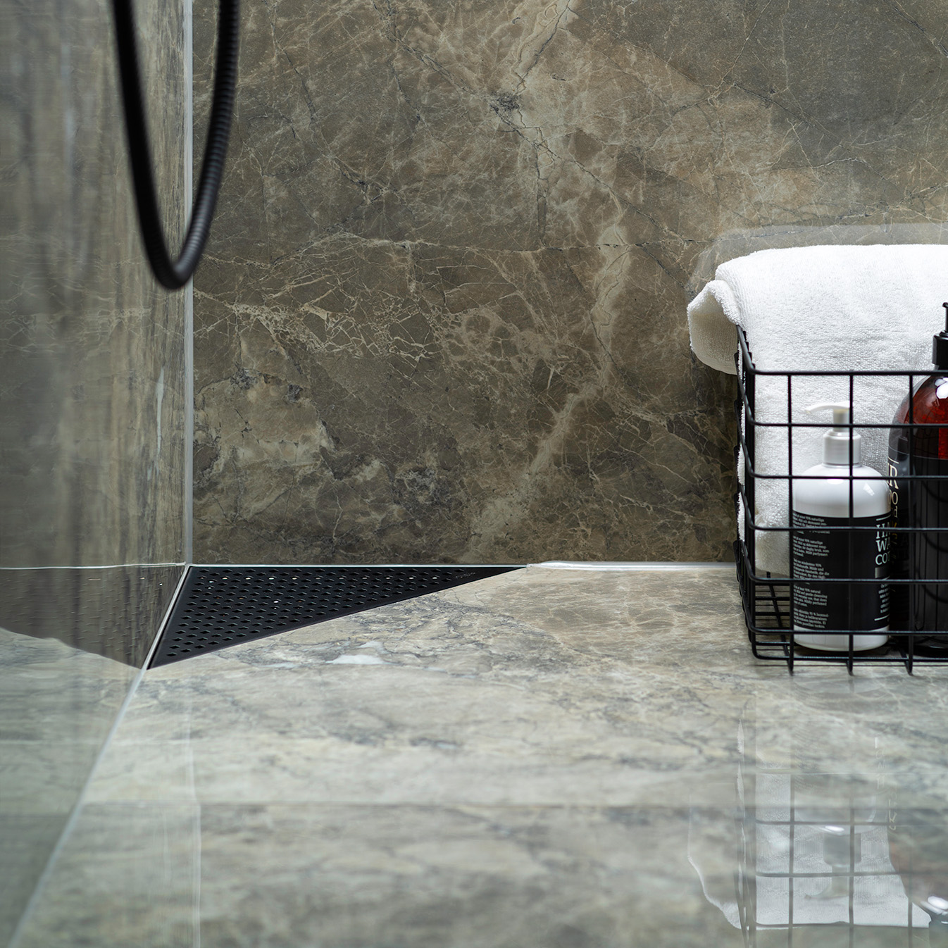 Et nærbilde av et matt svart Purus Corner hjørnesluk omgitt av brune marmorfliser, demonstrerer et elegant og funksjonelt designsluk egnet for mindre baderom.