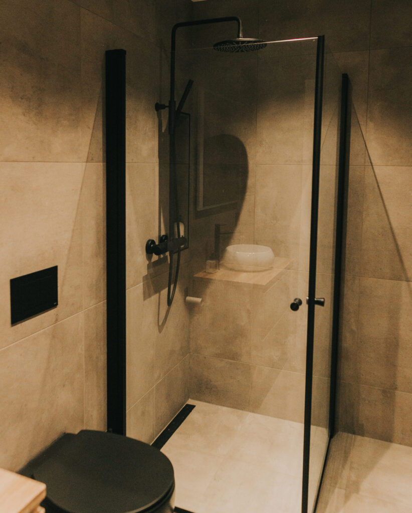 Mørkere baderom med deilig spafølelse og interiørdetaljer i matt svart - deriblant designsluket Purus Line Matt Svart montert inntil veggen i dusjen.
