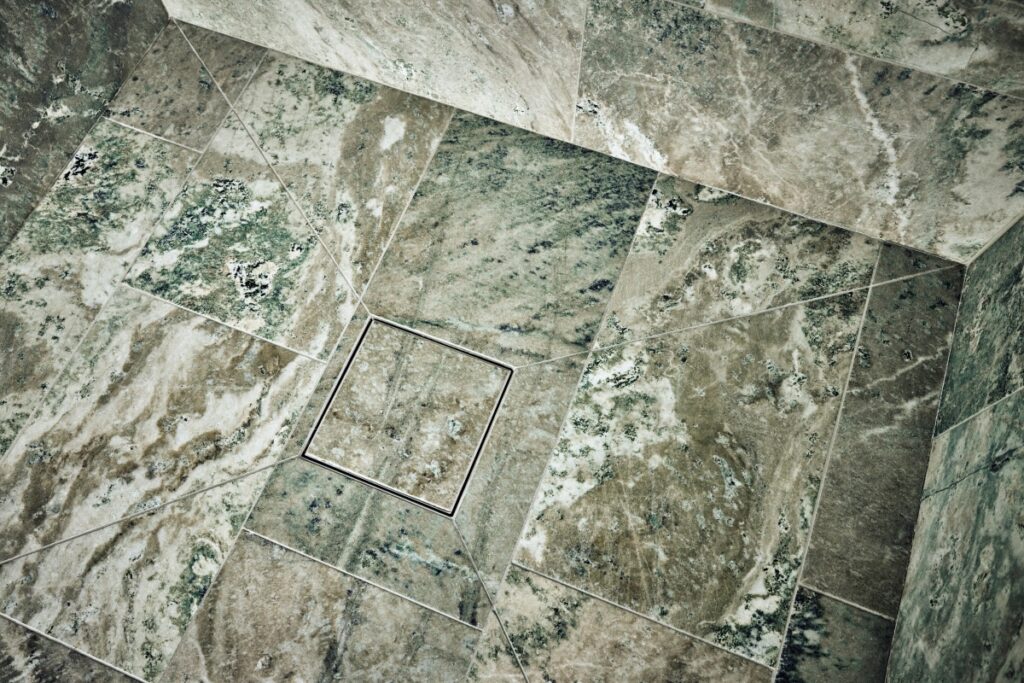 Flislagt dusjgulv i Kolmårdsmarmor med «pizzastykke»-kutt mot sluk, med Purus Square Tile Insert integrert i gulvet for et sømløst uttrykk.